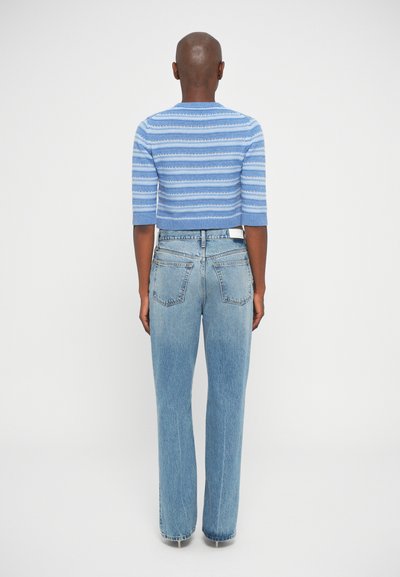 Pull en tricot bleu coupé avec des rayures horizontales, associé à un jean taille haute bleu clair, vu de l'arrière.