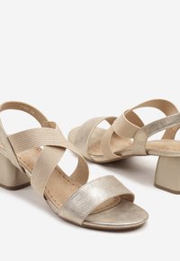 Sandales à talons dorées avec des lanières en élastique croisées et un dessus texturé. Design à bout carré et talon bloc avec une semelle intérieure douce.