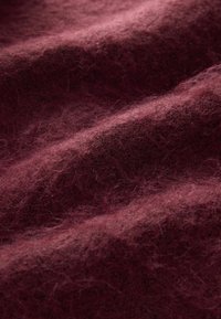 Bordeaux wolweefsel met een zachte, donzige textuur, gekenmerkt door zachte golven en variërende tinten diep rood, wat visuele diepte en warmte creëert.