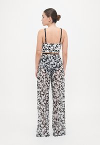 Completo a due pezzi con un top a fascia floreale bianco e nero con spalline sottili e pantaloni ampi trasparenti floreali abbinati.