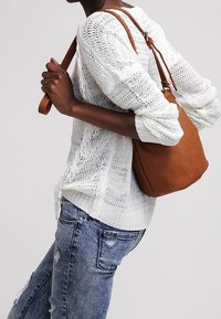 Braune Leder-Umhängetasche mit glatter Oberfläche, kombiniert mit einem leichten Strickpullover und verwaschenen blauen Jeans, was einen lässigen Look kreiert.