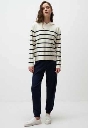 Felpa con cappuccio crema a strisce blu, abbinata a pantaloni blu a sigaretta e sneakers bianche. Tessuto morbido, vestibilità rilassata e polsini elasticizzati.