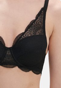 Soutien-gorge in pizzo nero con bordo ondulato, caratterizzato da un delicato motivo floreale, spalline regolabili e supporto con ferretto per migliorare la forma.