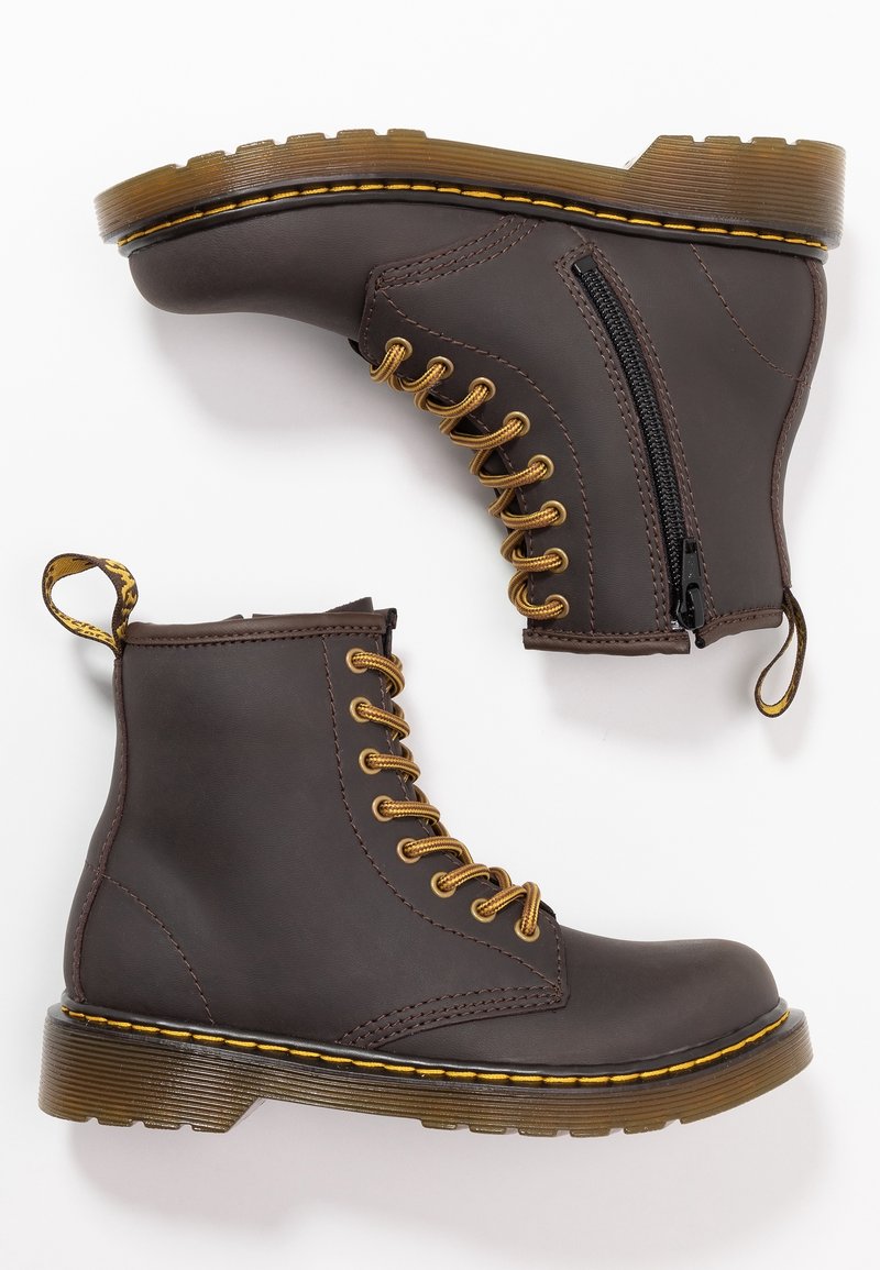 Paire de bottines en cuir marron foncé avec des lacets jaunes, des semelles épaisses translucides et des fermetures éclair latérales sur fond blanc.
