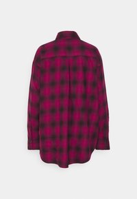 Chemise à manches longues boutonnée en flanelle à carreaux rose foncé et noir, vue de dos avec un pli central et des poignets boutonnés.