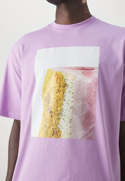 Paarse katoenen T-shirt met een grote afbeelding van een textuur, gelaagd stuk dat roze en gele tinten toont, omrand door wit.