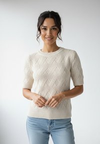 Kremowy sweter ze splotem kablownicowym z krótkimi rękawami, z fakturowanym wzorem i prążkowanym dekoltem. W połączeniu z jasnoniebieskimi dżinsami.
