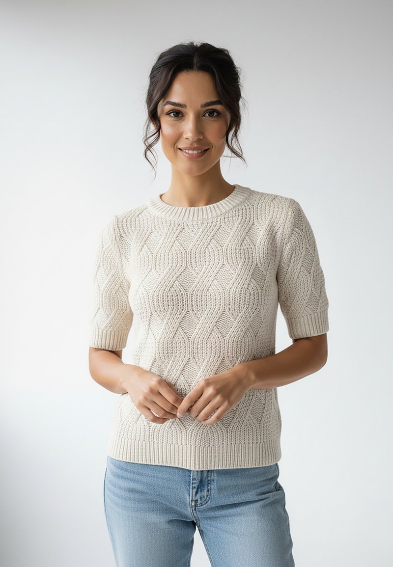 Kremowy sweter ze splotem kablownicowym z krótkimi rękawami, z fakturowanym wzorem i prążkowanym dekoltem. W połączeniu z jasnoniebieskimi dżinsami.