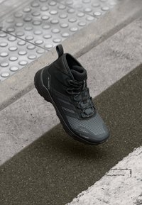 Schwarzer Wanderschuh mit einer strukturierten Mesh-Oberfläche, Gummisohle und erhöhten Akzenten. Verfügt über ein Schnürsystem und ein Logodetail an der Seite.