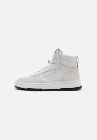 Sneaker alto bianco con accenti in suede beige, lacci bianchi, suola nera e un branding sottile sul lato, esposto su uno sfondo semplice.