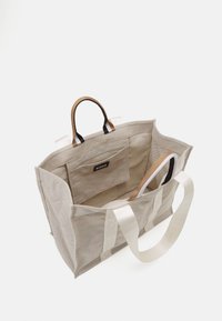Borsa tote in tela beige con un ampio interno, doppi manici superiori, una tasca interna e un'etichetta del marchio sul lato. Tracolla regolabile inclusa.