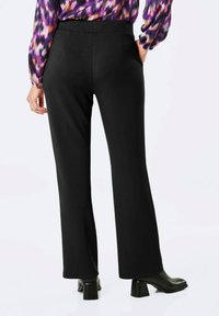 Zwarte flared broek met een soepele textuur, een middelhoog taille, en achterzakken, gecombineerd met zwarte hoge hakken en een gestreepte paarse blouse.