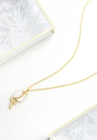 Guldkæde med en ros-formet vedhæng, der har en hvid sten og funklende krystaller på stilken. Enkel og elegant design.