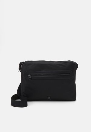Sac messager en nylon noir avec une poche zippée à l'avant, une bandoulière ajustable et un détail de logo. Texture lisse, forme rectangulaire, design minimaliste.