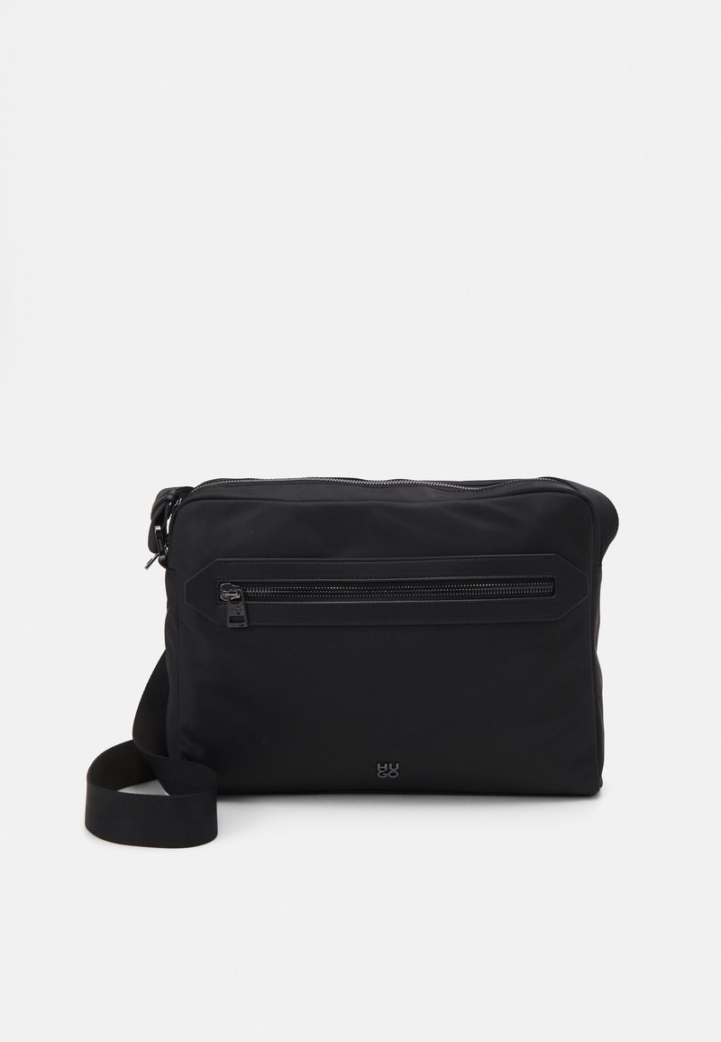 Sort nylon messenger taske med en frontlomme med lynlås, justerbar rem og logodetalje. Glat tekstur, rektangulær form, minimalistisk design.