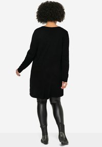 Black long-sleeve tunic with a relaxed fit, featuring a scoop neckline and side slits, paired with shiny black leggings and studded ankle boots.