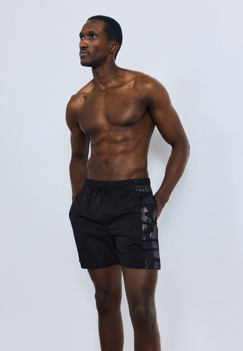 Μαύρο μαγιό με κορδόνι στη μέση, υφασμάτινες πλευρικές πινελιές με υφή και λείο φινίρισμα. Το ύφασμα φαίνεται ελαφρύ και γρήγορο στο στέγνωμα.