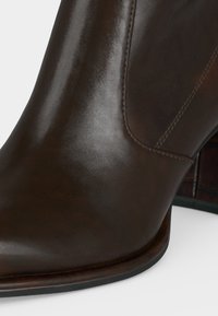 Gros plan d'une botte cheville en cuir marron foncé lisse avec détail de couture et talon bas empilé.