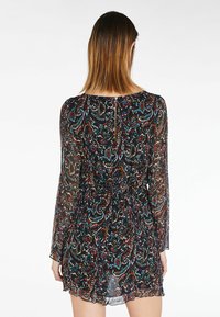 Schwarzes, transparentes Kleid mit Paisley-Muster in Rot, Blau und Weiß. Lange Ärmel, tailliert und mit Knopfverschluss am hinteren Halsausschnitt.