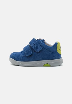 Blaues Wildleder-Kinderschuh mit zwei Klettverschlüssen, einer grauen Gummisohle und einem grünen Akzent an der Ferse, der ein Smiley-Gesichtsmotiv zeigt.