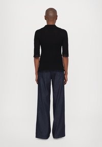 Top en tricot noir à manches courtes frangées, associé à un pantalon large en denim foncé à coupe ample.