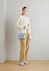 Světle béžový cardigan přes bílý top, široké kalhoty v barvě tan, světle modrá crossbody taška se zlatými detaily a světle modré klouzavé sandály.