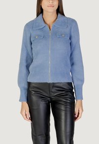 Maglione zip in blu chiaro realizzato in un materiale morbido e peloso, con design a collo, dotato di due tasche sul petto e dettagli in metallo dorato.
