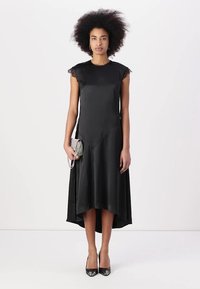 Svart satengkjole med blondebesatte cap-sleeves, asymmetrisk skjørtlinje og en glatt tekstur, kombinert med en glitrende clutch og høye hæler.