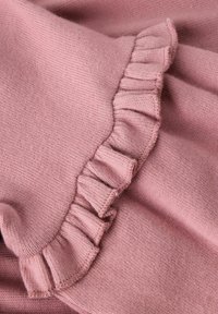 Růžová pletenina se zdobeným okrajem. Textura je měkká s jemně žebrovaným vzorem, který zvyšuje vrstvený vzhled designu.