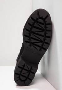 Suela de bota de goma negra con surcos profundos y acabado texturizado, que presenta una marca elevada y un borde suave.