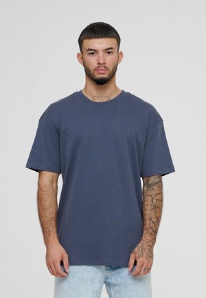 Tricou din bumbac de culoare albastru marin, cu mâneci scurte, guler rotund și o croială lejeră. Prezintă o textură netedă și un design casual.