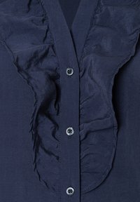 Chemise marine avec un plastron froncé, texture lisse et boutons ronds, dotée d'un col classique.