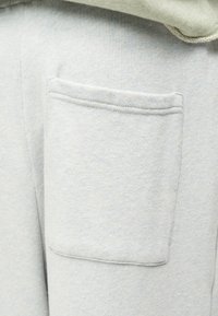 Κοντινή λήψη ανοιχτό γκρι ύφασμα που δείχνει μια ορθογώνια τσέπη με ραφές σε ένα απαλό ύφασμα ένδυσης.