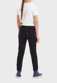 Jeans negros con un diseño ajustado, bolsillos delanteros y traseros, costuras dobles y una etiqueta del logo de Levi's en el bolsillo trasero derecho.