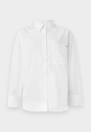 Biela košeľa s dlhým rukávom a gombíkmi vyrobená z bavlny. Funkcie klasického goliera, prednej vrecka a malého loga na vrecku.