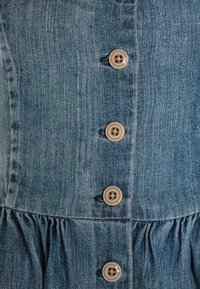 Abito in denim con corpino sfiancato e gonna arricciata, colore azzurro chiaro, cinque bottoni tondi marroni e una texture sottile.