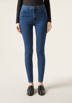 Jeans skinny in denim blu scuro, a vita alta con tasche frontali e passanti per cintura. Presentano una texture liscia e una leggera lucentezza.
