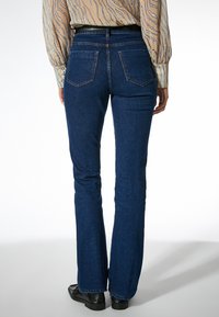 Jeans de mezclilla azul oscuro acampanados con detalles de costura sutiles, diseño de cinco bolsillos y cintura de altura media, combinados con una blusa estampada.