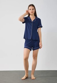 Mörkblå pyjamasset med kort ärm som inkluderar en knapp-upptill med vit kant och matchande shorts, tillverkad av mjukt material.