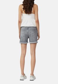 Shorts en denim gris avec des revers, dotés de deux poches arrière et d'une légère décoloration. Associés à un haut blanc fluide et des baskets.