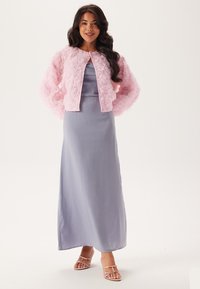 Lång lavendelfärgad satin klänning kombinerad med en fluffig rosa jacka i pälsstil med runda knappar och en strukturerad, kronbladsliknande design.