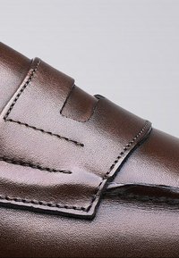 Bruine leren schoen met een gladde afwerking, voorzien van een decoratieve band en stiksels langs de rand.