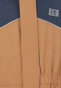 Tarnfarbener und marineblauer Jacke mit Reißverschluss, elastischem Bund und reflektierenden Akzenten. Verfügt über ein Etikett mit der Aufschrift "BEREIT ZUM SPIELEN".