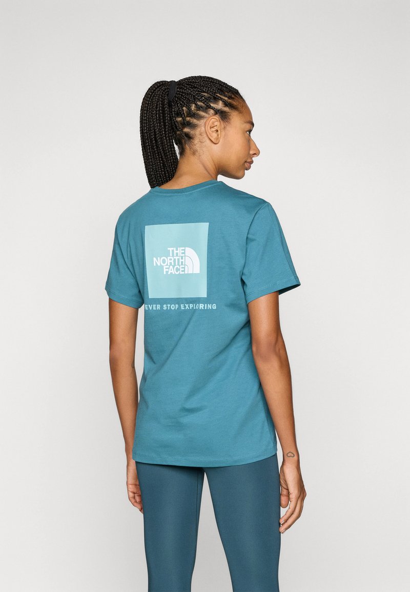 Teal pamučna majica s kratkim rukavima koja sadrži bijeli logotip The North Face na leđima, s okruglim izrezom.