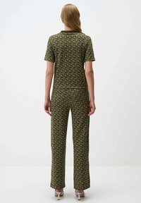 Zweiteiliges Outfit aus olivgrünem Stoff mit einem sich wiederholenden geometrischen Muster. Kurzärmliges Oberteil und lange, taillierte Hose.