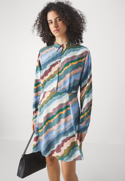 Abito a pulsante multicolore con un motivo ondulato in blu, verde, rosa e marrone. Maniche lunghe e vestibilità rilassata, abbinato a una borsa nera.