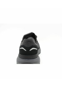 Sneaker nera con materiale testurizzato, design curvo e suola grigia. Dettagli notevoli includono una linguetta e il numero 19 stampato in rilievo.