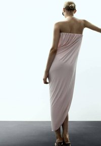 Sukienka bez ramiączek, do kostek, wykonana z miękkiego różowego materiału, z marszczonym materiałem w okolicy biustu i gładką, zwiewną sylwetką.