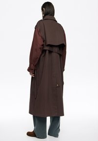 Długi, dwukolorowy trencz z brązową górną częścią i bordową dolną, uzupełniony paskiem i guzikami.