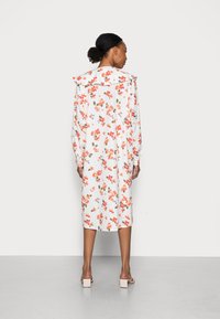 Vestido floral com base branca, apresentando flores vermelhas e azuis, mangas longas e um grande colarinho; usado com sandálias de salto bloco claro.